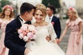 Handsome groom in suit hugging elegant blonde bride with bridesmaids and groomsmen