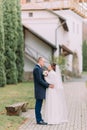 Handsome groom tenderly embracing his tender bride at stroll in green park with ancient buildings and cypress trees Royalty Free Stock Photo