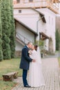 Handsome groom tenderly kissing his tender bride at stroll in green park with ancient buildings and cypress trees Royalty Free Stock Photo