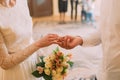 Handsome groom in white shirt putting wedding ring on stylish bride at registry, close-up