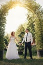 Handsome groom holds the bride`s hand near green flower archway Royalty Free Stock Photo