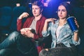 Handsome guy and beautiful girl are sitting together and watching movie. Their right hands are posing. Girl is holding a Royalty Free Stock Photo