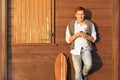 Handsome guy in four season outfit standing on brown wooden background and holding his smartphone - Smiling men in autumn clothes Royalty Free Stock Photo