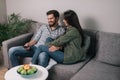 Handsome guy and girl is watching TV together sitting on soft gray couch Royalty Free Stock Photo