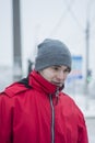 A handsome guy in a gray hat and a red jacket. He looks away, incredulously. Winter. Close-up portrait of a young guy. Brunette wi