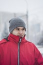 A handsome guy in a gray hat and a red jacket. He looks away, incredulously. Winter. Close-up portrait of a young guy. Brunette wi