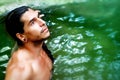 A handsome guy with long hair and piercings on waterfalls in a rain forest against a background of green water