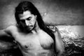 A handsome guy with long hair and piercings on waterfalls in a rain forest. Tarzan concept. Black and white photo. Royalty Free Stock Photo