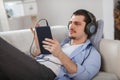 Handsome guy lying on sofa with tablet and headphones Royalty Free Stock Photo