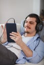 Handsome guy lying on sofa with tablet and headphones Royalty Free Stock Photo