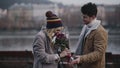 Handsome guy mading date with pretty blonde on river embankment on summer, spring or autumn day, presenting bouquet of