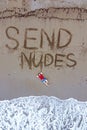 Handsome guy in red t-shirt and blue male boxers is lying on beach washed by foaming sea waves. send nudes inscription on wet sand