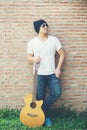 Handsome guy standing holding guitar against the brick wall posing look away. Relaxing holiday.