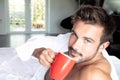 Handsome hairy naked muscular man with beard sixpack abs lying in bed covered with sheet drinking coffee Royalty Free Stock Photo