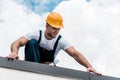 Handyman in yellow helmet and uniform repairing roof