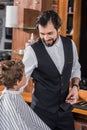 handsome happy barber talking to little kid while he sitting in chair