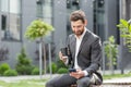 Handsome happy bearded businessman sitting on bench with cup coffee use mobile phone browse smartphone in hands reads good news Royalty Free Stock Photo