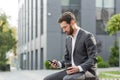 Handsome happy bearded businessman sitting on bench with cup coffee use mobile phone browse smartphone in hands reads good news Royalty Free Stock Photo