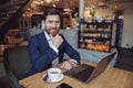 Handsome happy Caucasian successful businessman sitting at laptop, smiling in cafe. Royalty Free Stock Photo