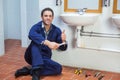 Handsome happy plumber sitting next to sink showing thumb up