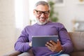 Handsome happy senior man using digital tablet while relaxing resting on sofa at home Royalty Free Stock Photo