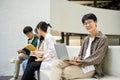 Handsome Asian male college student sits on a bench at a campus relaxation area with his laptop Royalty Free Stock Photo