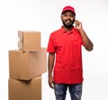 Handsome happy young delivery man talking by mobile phone in red cap standing with parcel post boxes isolated over white Royalty Free Stock Photo