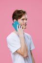 handsome happy young man teenager in white t-shirt stands talking on the phone in blue case looking at camera on pink