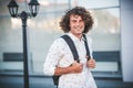 Handsome happy young student guy with backpack on the city street. Caucasian male with curly hair, smiling and looking at the Royalty Free Stock Photo