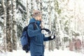 Handsome hiker man in warm clothes with backpack pours tea in mug from thermos in winter forest. Season concept. Copy space