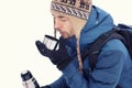 Handsome hiker man in warm clothes drinking tea in mug from thermos in winter forest. Season concept