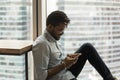 Hipster African guy sit in modern apartment with smartphone Royalty Free Stock Photo