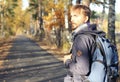 Handsome hipster man with backpack walking on the autumn park. D