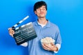 Handsome hipster young man eating popcorn holding cinema clapboard looking at the camera blowing a kiss being lovely and sexy Royalty Free Stock Photo