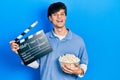 Handsome hipster young man eating popcorn holding cinema clapboard smiling with a happy and cool smile on face Royalty Free Stock Photo