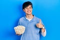 Handsome hipster young man eating popcorn smiling happy and positive, thumb up doing excellent and approval sign Royalty Free Stock Photo