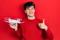 Handsome hipster young man holding drone smiling happy and positive, thumb up doing excellent and approval sign Royalty Free Stock Photo