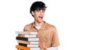 Handsome hipster young man holding a pile of books winking looking at the camera with sexy expression, cheerful and happy face Royalty Free Stock Photo