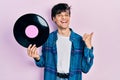 Handsome hipster young man holding vinyl disc pointing thumb up to the side smiling happy with open mouth Royalty Free Stock Photo