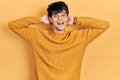 Handsome hipster young man wearing casual yellow sweater relaxing and stretching, arms and hands behind head and neck smiling Royalty Free Stock Photo