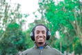 Handsome hispanic black man wearing green sweater in outdoors park area, headphones on covering ears and smiling Royalty Free Stock Photo