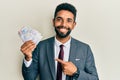 Handsome hispanic business man with beard holding swedish krona banknotes smiling happy pointing with hand and finger Royalty Free Stock Photo