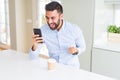 Handsome hispanic business man drinking coffee and using smartphone screaming proud and celebrating victory and success very