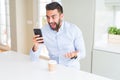 Handsome hispanic business man drinking coffee and using smartphone very happy and excited, winner expression celebrating victory Royalty Free Stock Photo