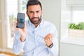 Handsome hispanic business man showing smartphone screen annoyed and frustrated shouting with anger, crazy and yelling with raised Royalty Free Stock Photo