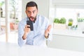 Handsome hispanic business man using smartphone very happy and excited, winner expression celebrating victory screaming with big Royalty Free Stock Photo