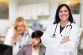 Happy Hispanic Doctor or Nurse Standing in Her Office with Staff Working Behind Royalty Free Stock Photo
