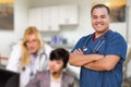 Handsome Hispanic Doctor or Nurse Standing in His Office with Staff Working Behind