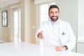 Handsome hispanic doctor or therapist man wearing medical coat at the clinic smiling friendly offering handshake as greeting and Royalty Free Stock Photo