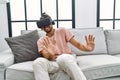 Handsome hispanic man afraid wearing virtual reality glasses at the living room at home